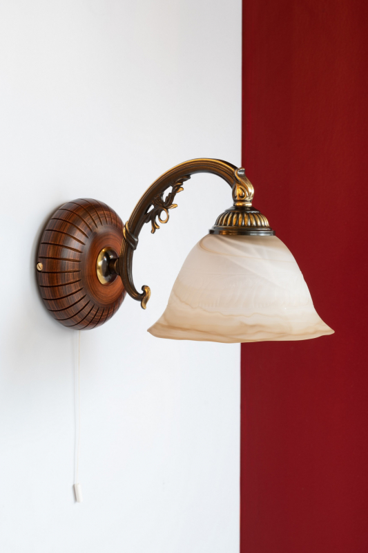 Lampada da muro classica in fusione di ottone, color Bronzo Sfumato. Vetro satinato tabacco. Legno inciso decoro antico. Prodotto in Italia. Codice A.5921/1.
